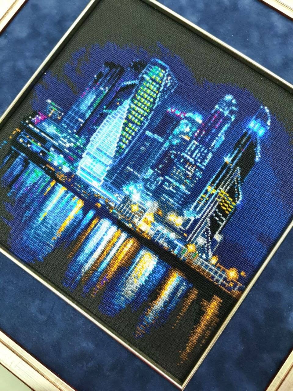 Kit de punto de cruz RIOLIS Ciudad Nocturna con rascacielos iluminados y reflejos sobre el mar en una vista nocturna panorámica.