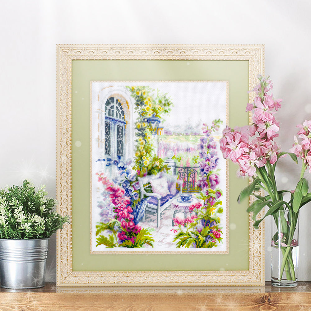 Cuadro Bordado en punto de cruz de una acogedora terraza con flores en tonos lilas y rosas de Magic Needle