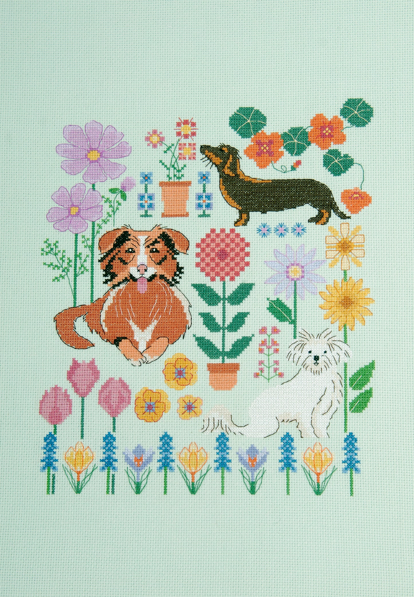 Kit de punto de cruz DMC “Perros en el Jardín” de Marie-Dominique Procureur con perros entre flores veraniegas bordado en tela Aida 14 ct.