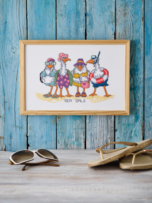 Kit de punto de cruz Permin Gaviotas en la Playa con cuatro gaviotas vestidas con ropa veraniega sobre la arena, incluye tela Aida blanca, hilos, aguja e instrucciones.