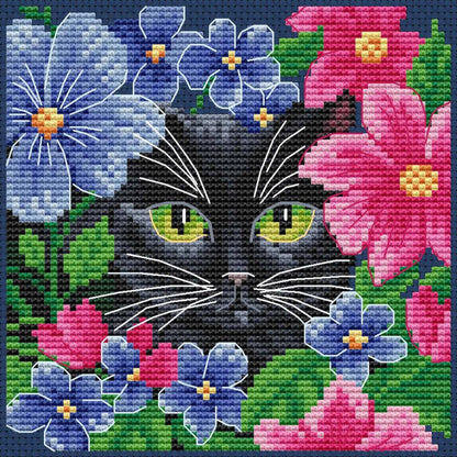 Kit de punto de cruz Collection D'Art "Gato Entre Flores" con gato negro rodeado de flores de colores. Incluye tela Aida, hilos DMC, aguja e instrucciones.