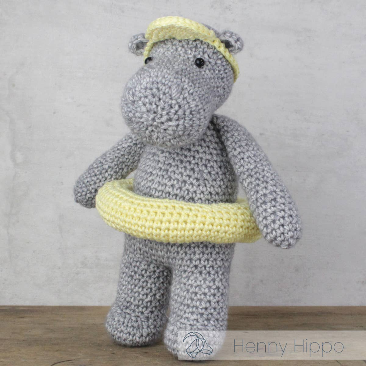 Kit de ganchillo Hardicraft Henny Hippo con amigurumi de hipopótamo tejido en tonos gris y amarillo, ideal como decoración infantil o regalo hecho a mano.