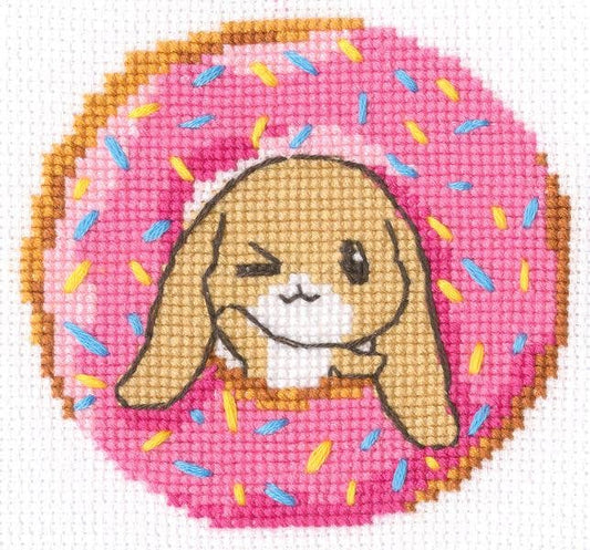 Kit de punto de cruz infantil RTO "Conejito con Donut Rosa" con conejito dentro de un donut rosa. Incluye tela, hilos DMC, aguja e instrucciones.