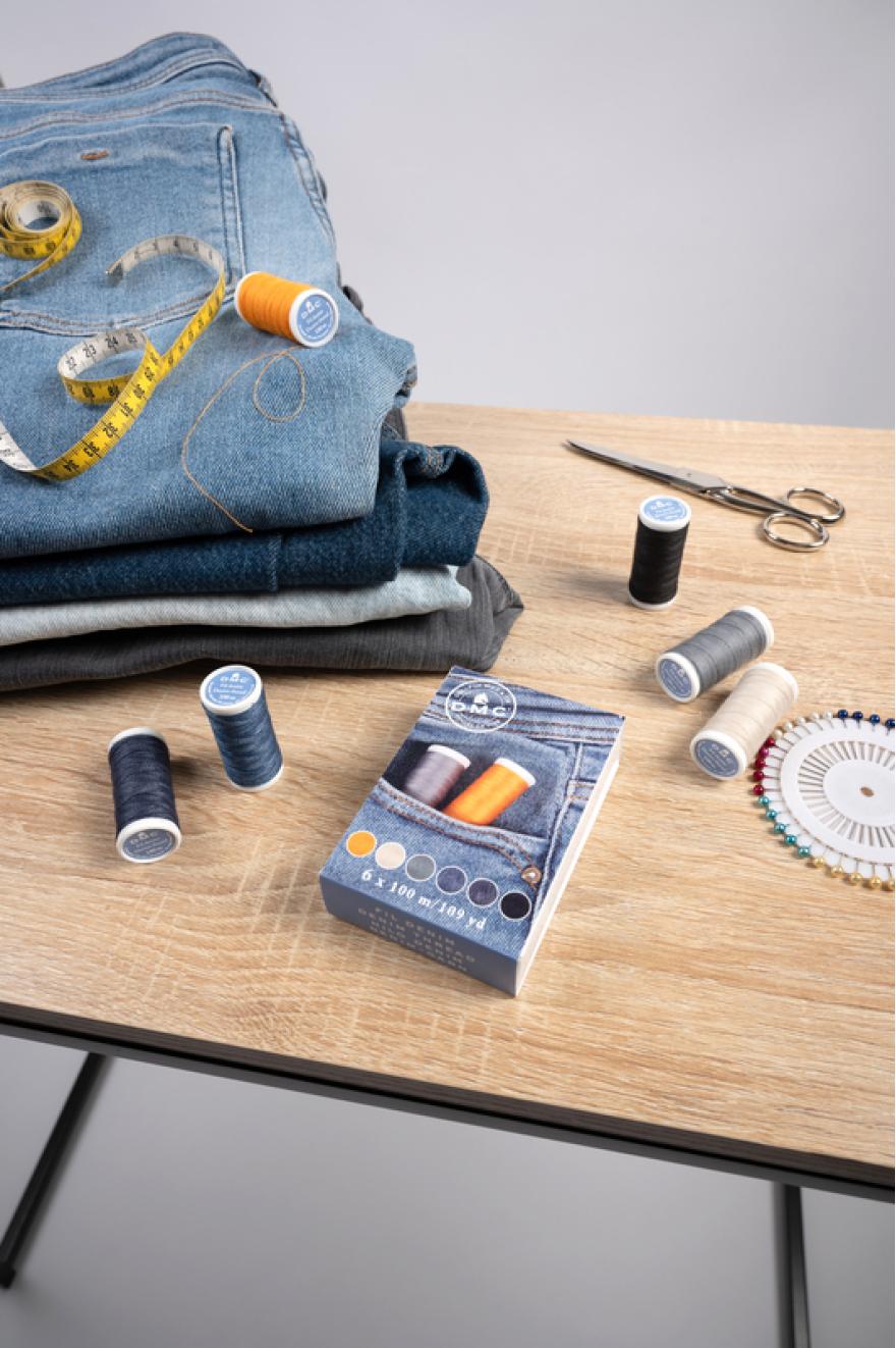 Hilos de coser DMC para reparación de jeans junto a vaqueros, tijeras y accesorios de costura