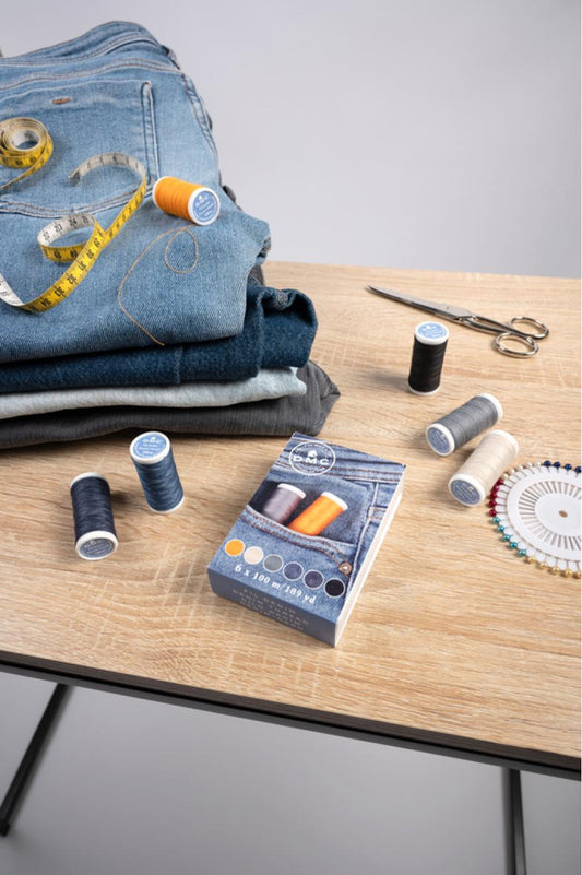 Hilos de coser DMC para reparación de jeans junto a vaqueros, tijeras y accesorios de costura