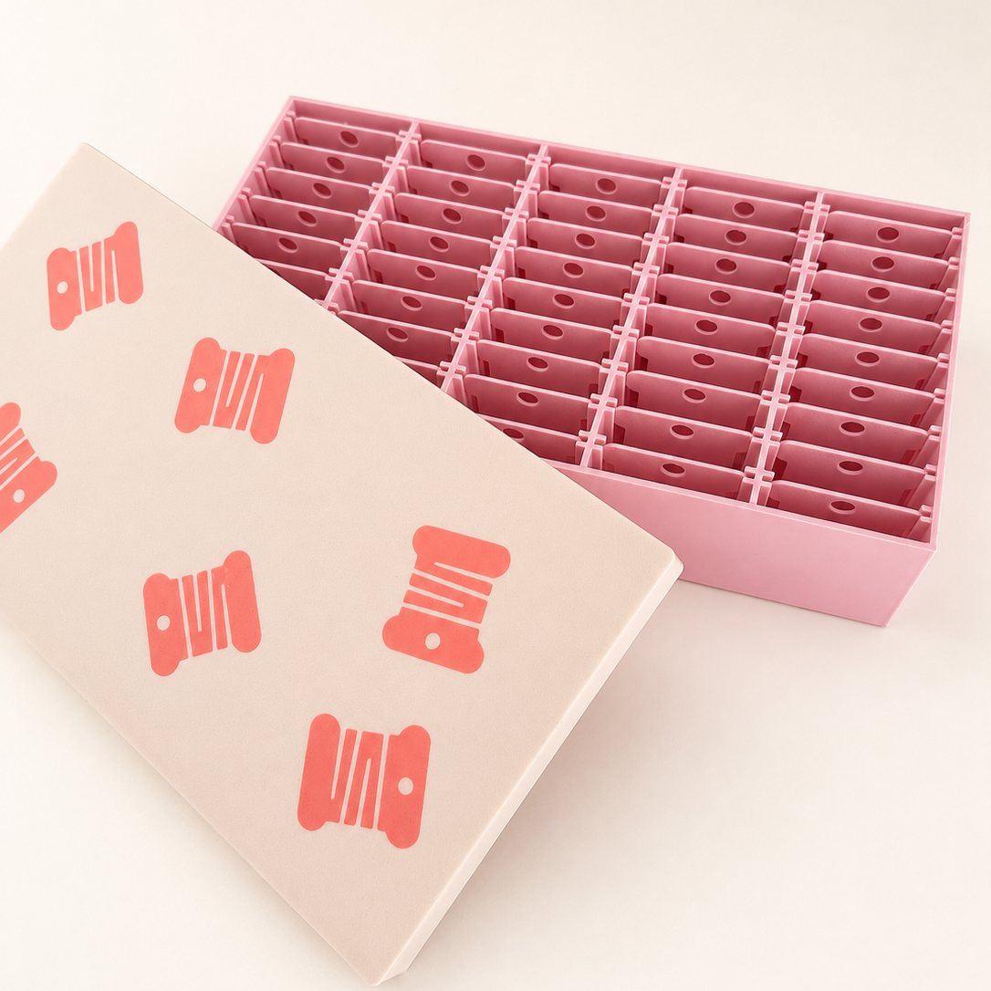 Caja organizadora rosa y beige abierta con 45 espacios para bobinas de hilo