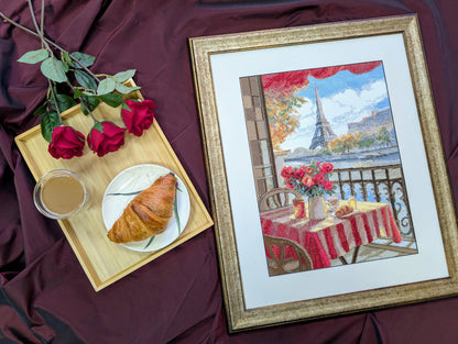 Kit de punto de cruz Aine París Soleado con escena de terraza parisina, mesa con desayuno, flores y Torre Eiffel de fondo.