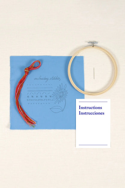 Contenido del kit de iniciación al bordado DMC con tela impresa azul, hilos, aguja, bastidor e instrucciones