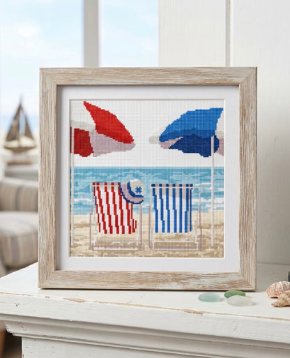 Kit de punto de cruz Dúo Junto al Mar de Marie Coeur con diseño marinero de tumbonas, sombrillas, playa y mar en tonos azules y rojos.