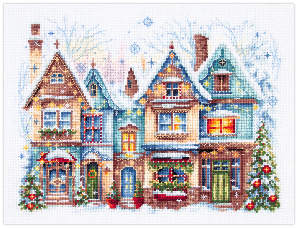 Kit de punto de cruz Magic Needle Heartwarming con diseño navideño de casas iluminadas, guirnaldas y árboles de Navidad en estilo invernal.