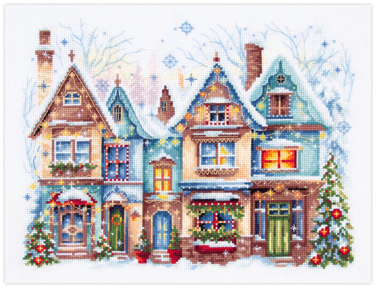 Kit de punto de cruz Magic Needle Heartwarming con diseño navideño de casas iluminadas, guirnaldas y árboles de Navidad en estilo invernal.
