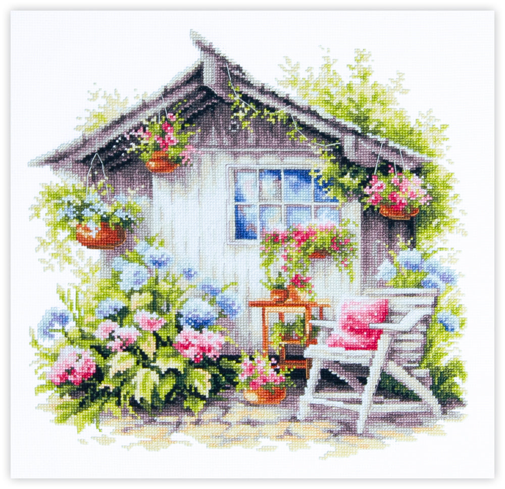 Kit de punto de cruz Quiet Happiness con casita de jardín, flores y silla en escena tranquila y acogedora.
