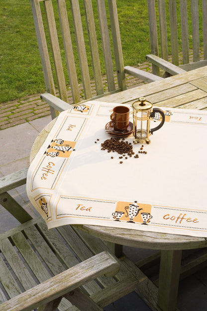 Kit punto de cruz mantel Tea and Coffee de Vervaco sobre mesa de jardín con tazas y granos de café