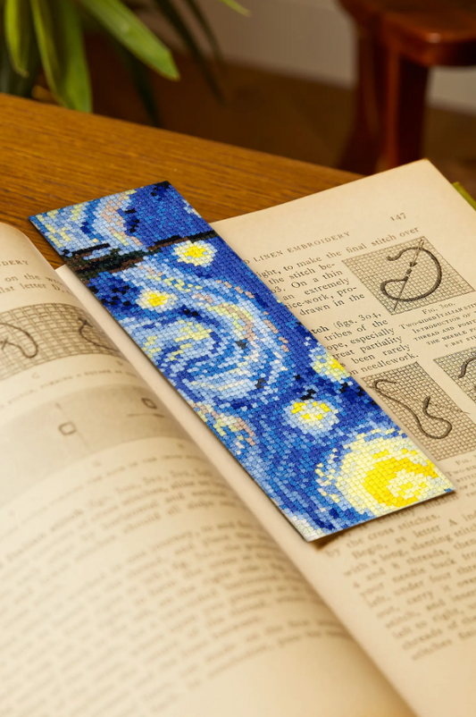 Kit de punto de cruz DMC para crear un marcapáginas inspirado en La noche estrellada de Van Gogh. Incluye hilos, tela Aida, aguja, soportes e instrucciones.