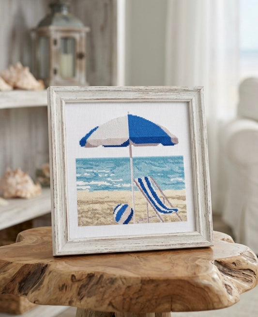 Kit de punto de cruz Orilla del Mar en Azul de Marie Coeur con tumbona azul, sombrilla, pelota de playa y paisaje costero.