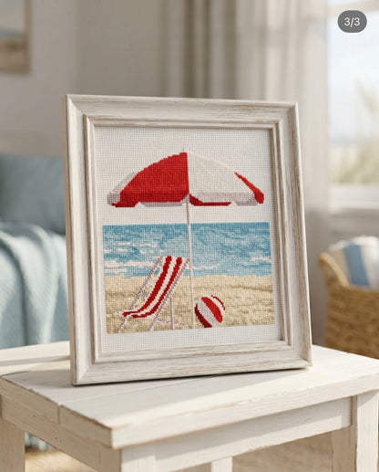 Kit de punto de cruz Orilla del Mar en Rojo de Marie Coeur con tumbona roja, sombrilla, pelota de playa y paisaje costero.