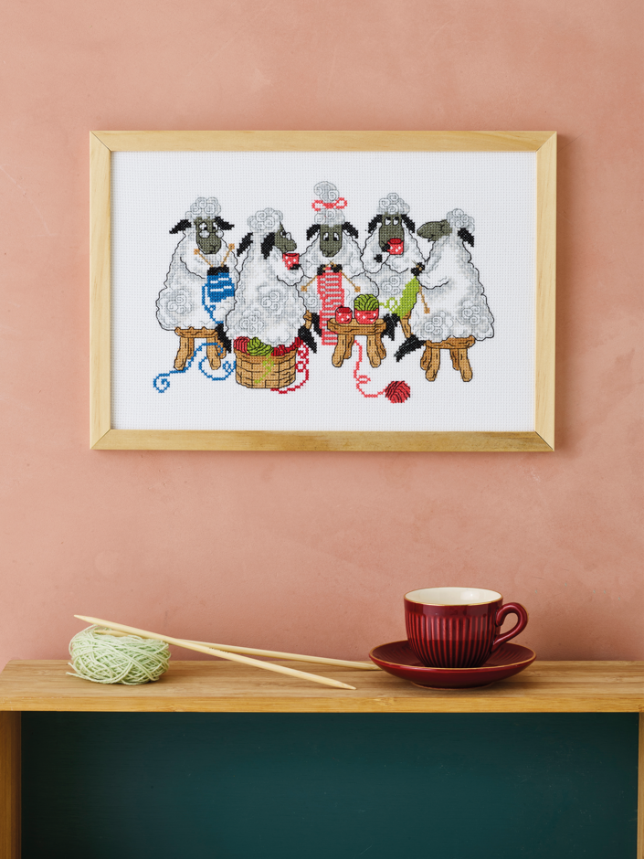 Kit de punto de cruz Permin Ovejas Crocheteras con grupo de ovejas tejiendo con ovillos de colores sobre tela Aida blanca, incluye hilos, aguja e instrucciones.