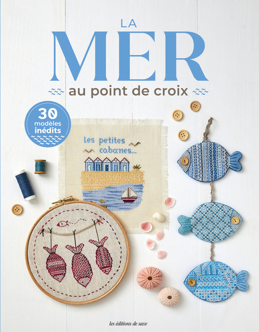 Portada del libro “La mer au point de croix: 30 modèles inédits” de Les Éditions de Saxe con motivos marinos bordados: peces, casitas de playa y bastidor decorativo.