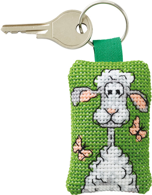 Kit de punto de cruz Permin llavero oveja blanca con mariposas rosas sobre fondo verde, incluye tela Aida, hilos, aguja, anilla e instrucciones.
